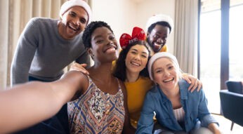 Gruppe junger Erwachsener im Wohnzimmer macht Selfie mit Weihnachts-Mützen