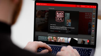 Mann sitzt vor MacBook Pro und hat die Finger auf der Tastatur, im Display ist die featured-Homepage zu sehen.