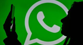 Silhouette einer Frau mit Smartphone vor dem WhatsApp-Logo