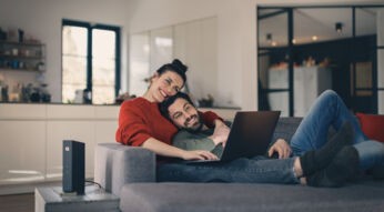 Ein Paar sitzt gemütlich auf der Couch mit einem Laptop auf dem Schoß