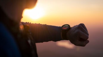 Ein junger Herr blickt auf seine Smartwatch, bei Sonnenuntergang.