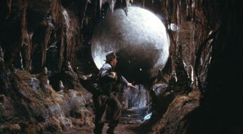 Indiana Jones (Harrison Ford) läuft vor einer Steinkugel weg, die ihn droht zu erdrücken in einem der besten Filme von George Lucas