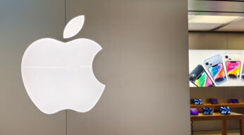 Beleuchtetes Apple Logo im Vordergrund, im Hintergrund Apple Store mit iPhones