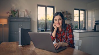 Frau sitzt am Tisch mit Laptop und Kabelrouter von Vodafone steht auf dem Tisch