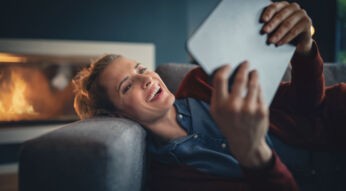 Lachende Frau liegt auf dem Sofa mit ihrem Tablet in der Hand
