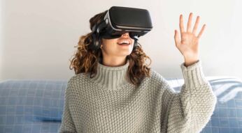 Eine Frau trägt eine VR-Brille und sitzt auf einem Sofa