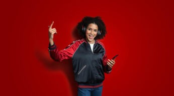 Auf dem Bild zum Deezer Angebot bei Vodafone siehst Du eine fröhlich lächelnde Person mit Kopfhörern, die ein Smartphone in der Hand hält und zur Musik zu tanzen scheint.