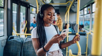 Junge Frau im Bus hört Musik und schaut lächelnd auf ihr Handy