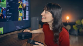 Bei der Auswahl der Vodafone Premium Plus Sender blickt eine junge Frau lächelnd auf den Fernseher, während sie eine Fernbedienung in der Hand hält.