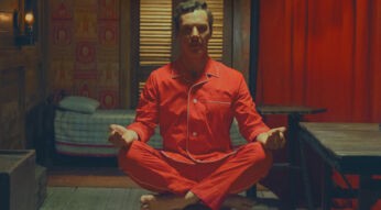 Ein Mann in einem roten Pyjama sitzt im Schneidersitz auf einem Hocker.