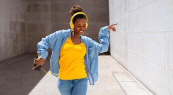 Junge FRau mit Smartphone und Kopfhörer tanzt.