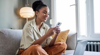 Eine junge Frau sitzt mit ihrem Smartphone in den Händen auf der Couch