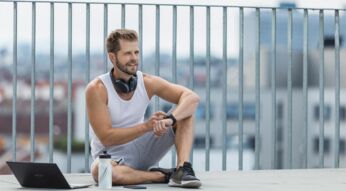 Junger Mann sitzt mit Laptop und Smartwatch auf einer Dachterasse