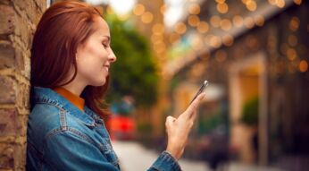Eine junge Frau schaut auf ihr Handy und lächelt dabei.