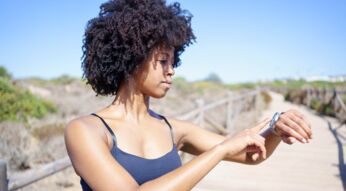 Junge Frau im Freien guckt auf ihre Smartwatch am Handgelenk