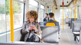 Eine junge Frau sitzt in einem Bus und schaut auf ihr Handy.