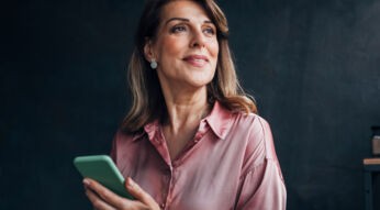 Eine Frau hält ihr Smartphone in der Hand und lächelt