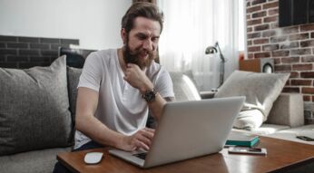 Ein Mann sitzt auf der Couch und nutzt dabei einen Laptop auf dem Tisch vor sich.
