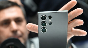 Hand greift nach einem Smartphone im Vordergrund, im Hintergrund das Gesicht eines Mannes