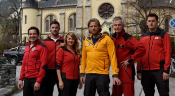 Fünf Männer und eine Frau stehen vor einer Kirche, sie tragen Uniformen des Bergrettungsdienstes