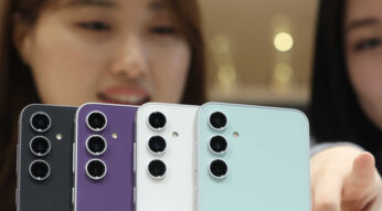 Vier Farbversionen des Galaxy S23 FE von hinten nebeneinander, im Hintergrund zwei Frauenköpfe