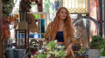 Das Szenenbild aus dem Film Nur noch ein einziges Mal im Artikel zu den besten Filmen und Serien mit Blake Lively zeigt die Hauptfigur Lily, gespielt von Blake LIvely in der Bildmitte. Sie steht in ihrem Blumenladen: Um sie herum stehen Blumrntöpfe, bunte Fensterglasscheiben in Holzrahmen und ein paar Pflanzen. Der untere mittige Bildrand wird von einer Pflanze verdeckt, die unscharf im Bild ist. Lily trägt ein offenes gelb-beige gestreiftes Hemd, darunter ein schwarzes Top und eine Jeans. Ihre langen, blonden Haare fallen ihr über die Schultern. Sie blickt an der Kamera vorbei und scheint jemandem zuzulächeln.
