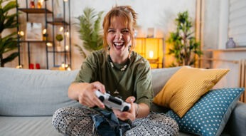 Eine Frau sitzt auf dem Sofa und spielt an der Konsole mit einem Controller