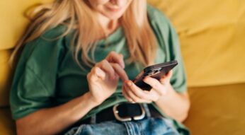 Frau sitzt mit iPhone in der Hand auf dem Sofa