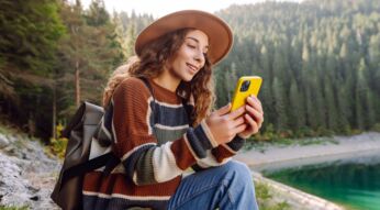 Frau schaut auf ihr iPhone, während sie an einem großen See sitzt.