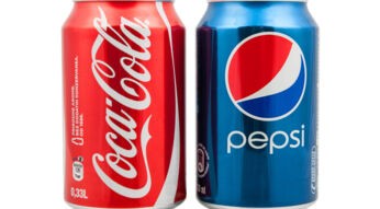 Auf diesem Bild zur "Cola Wars: Wahre Geschichte" stehen eine rote Coca-Cola-Dose und eine blaue Pepsi-Dose nebeneinander. Die Coca-Cola-Dose links trägt das ikonische weiße Logo auf rotem Hintergrund, während die Pepsi-Dose rechts das moderne Logo auf blauem Grund zeigt. Beide Dosen haben ein Volumen von 0,33 Litern und stehen symbolisch für den langjährigen Wettbewerb der beiden Marken.