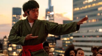 Auf dem Karate Kid: Legends-Bild siehst du Li Fong (Ben Wang), der in einer Kampfpose steht. Er trägt einen traditionellen Karate-Gi in Grün mit einem roten Gürtel und hält seinen rechten Arm ausgestreckt, während seine linke Hand vor der Brust positioniert ist.