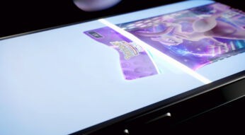 Auf dem Bild zu dem Artikel über die Pokémon TCG Pocket Tipps ist ein Smartphone-Display zu sehen, auf dem eine holografische Pokémon-Karte erscheint. Die Karte schimmert in violettem Licht, während das Logo von Pokémon Trading Card Game hervorgehoben ist. Das Smartphone liegt leicht angewinkelt auf einer dunklen Oberfläche, wodurch der futuristische Effekt der Darstellung betont wird.
