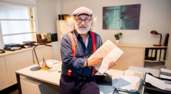 Klaus-Peter Wolf sitzt auf dem Schreibtisch der Hauptkommissarin Ann Kathrin Klaasen aus den Ostfriesenkrimis