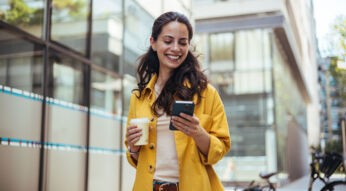 Eine Frau hält einen Kaffee und ein Handy in der Hand