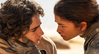 Auf dem Bild zu einem der besten Filme 2024, Dune 2, sind Paul Atreides, gespielt von Timothée Chalamet, und Chani, dargestellt von Zendaya, in einer intensiven Szene zu sehen. Paul blickt mit geschlossenen Augen nach unten, während Chani ihn ernst und eindringlich ansieht. Sie hält vorsichtig sein Gesicht mit einer behandschuhten Hand. Der Hintergrund zeigt eine helle, wüstenartige Landschaft.