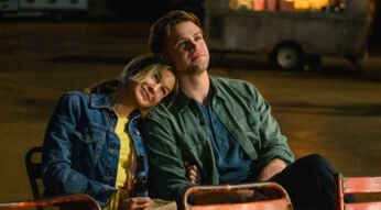 Auf dem Bild aus Bridget Jones 4 sind Bridget Jones, gespielt von Renée Zellweger, und Roxter, dargestellt von Leo Woodall, zu sehen. Bridget lehnt sich entspannt an Roxters Schulter, beide wirken ruhig und zufrieden. Sie sitzen in einer nächtlichen Outdoor-Szene auf einfachen Stühlen, während Bridget eine Bierflasche in der Hand hält. Im Hintergrund ist eine unscharfe Umgebung mit einem Anhänger und warmem Licht zu erkennen.