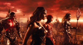 In dieser Szene aus dem DC Universum ist Gal Gadot als Wonder Woman im Vordergrund zu sehen, in ihrer ikonischen goldenen Rüstung. Links von ihr steht ein Cyborg-ähnlicher Charakter, während Jason Momoa als Aquaman ganz rechts mit seinem Dreizack abgebildet ist. Im Hintergrund erscheint ein Charakter in rotem Anzug. Der Himmel ist in dramatischen Rottönen gehalten und vermittelt eine bedrohliche Stimmung.