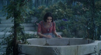 In einer Szene aus der Schneewittchen Realverfilmung ist Schneewittchen an einem steinernen Brunnen zu sehen. Sie trägt ein rotes Oberteil mit blauem Kleid und beugt sich über den kunstvoll verzierten Brunnenrand.