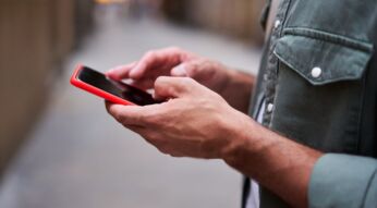 Zwei Hände halten ein Android-Handy mit roter Hülle.