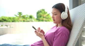 Frau im lila Shirt mit Kopfhörern schaut auf ihr Smartphone