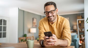 Ein Mann stützt sich mit den Ellbogen auf einer Kücheninsel ab und schaut dabei auf sein Smartphone.