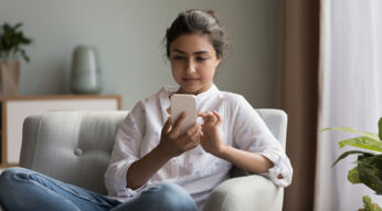 Eine junge Frau sitzt auf einem Sofa und bedient ihr Smartphone.
