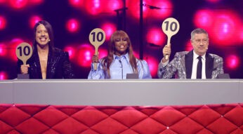 Auf dem Bild in dem Artikel zu den Let's Dance Gewinner:innen ist die Jury der Show zu sehen. Die drei Juror:innen halten jeweils eine Tafel mit der Zahl 10 hoch. Links sitzt ein Juror in einem schwarzen, glitzernden Outfit, in der Mitte eine Jurorin in einem auffälligen, hellblauen Kleid, und rechts ein Juror in einem silbernen, funkelnden Sakko. Der Hintergrund leuchtet in kräftigen Pinktönen, was die festliche Atmosphäre unterstreicht.