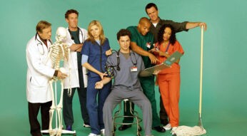 Auf dem Bild zum Scrubs Reboot sind die Hauptcharaktere aus der Serie in einer humorvollen Gruppenaufnahme zu sehen. Von links nach rechts stehen Dr. Bob Kelso (Ken Jenkins) mit einem Skelett, Dr. Cox (John C. McGinley) mit verschränkten Armen, Dr. Elliot Reid (Sarah Chalke) in blauer Kleidung, J.D. (Zach Braff) sitzend mit Stethoskop, Turk (Donald Faison) in grüner Kleidung, der Hausmeister (Neil Flynn) mit einem Wischmopp und Carla (Judy Reyes) in orangefarbener Kleidung. Die Szene ist lebendig und voller Witz.