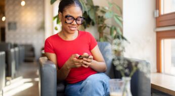 Lächelnde Frau mit roten T-Shirt schaut lächelnd auf ihr Smartphone, das sie in den Händen hält.