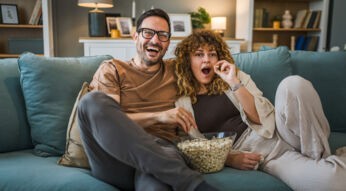 Ein Mann und eine Frau sitzen auf einem Sofa, essen Popcorn und schauen Tv
