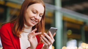 Eine junge Frau schaut auf ihr Smartphone und tippt etwas ein.