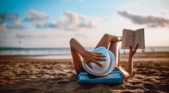 Eine Frau liest am Strand liegend ein Buch.