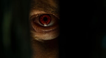 Ein unheimliches, rot leuchtendes Auge blickt durch einen schmalen Spalt. Die düstere Beleuchtung und der intensive Blick erzeugen eine bedrohliche Atmosphäre, die an Szenen aus Monsterfilmen erinnert. Der Fokus liegt auf dem Auge, das fast übernatürlich wirkt.