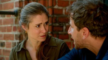 Auf dem Bild aus Rote Rosen sind die Darsteller:innen Lea Marlen Woitack als Svenja und Vivian Frey als Arthur zu sehen. Die Szene zeigt ein intensives Gespräch zwischen den beiden. Svenja blickt Arthur mit ernster Miene und leicht besorgtem Ausdruck an, während er spricht. Der Hintergrund mit rotem Ziegelmauerwerk verleiht der Szene eine warme, aber zugleich angespannte Atmosphäre.